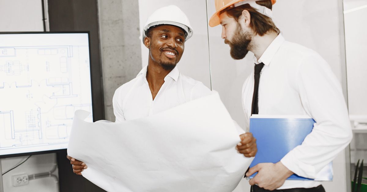 Two architects in hard hats discuss blueprints in a modern office setting, highlighting teamwork and planning.