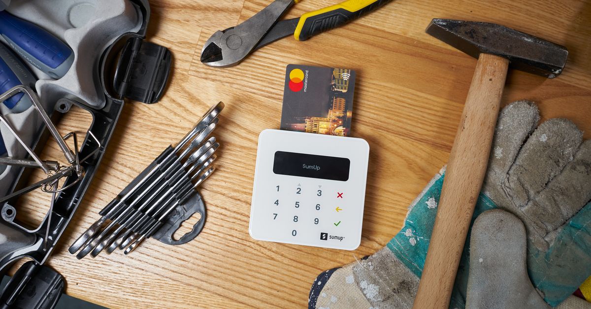 Overhead view of bright small plastic card in white contemporary wireless cash register surrounded by screwdriver set and hammer on big dirty gloves next to pliers